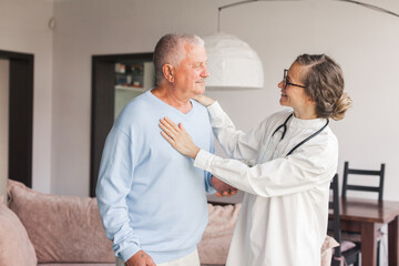 Female professional doctor showing medical test result explaining prescription using clipboard visiting senior elderly old man patient at home sitting on sofa