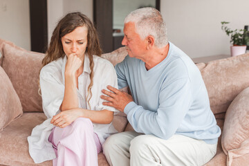 Worried aged father embracing comforting sad grown up daughter with broken heart family sit on sofa