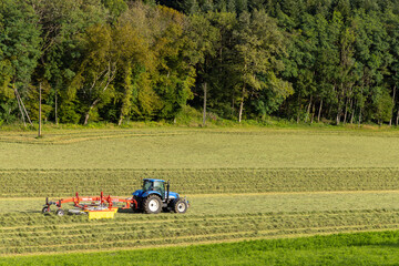 Tractor turning hay in spring meadow, Jura, France