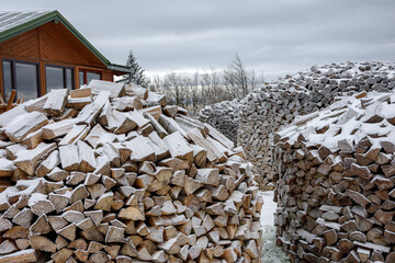 Concept of traditional preparing firewood for winter by putting it in piles near a mountain wooden cottage.