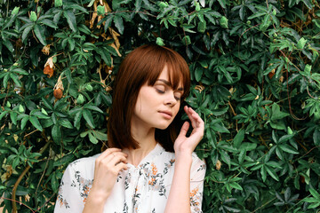 Serene woman with eyes closed leaning against lush greenery in peaceful contemplation