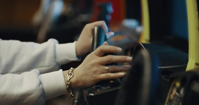 Woman hands holding a steering wheel while playing a driving simulation game at a vibrant arcade, conveying a sense of fun and relaxation.