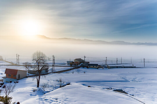 Sunrise through fog over a peaceful, rural snowy landscape (Togari, Nagano)