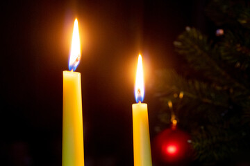 two lit candles near the Christmas tree on a dark background
