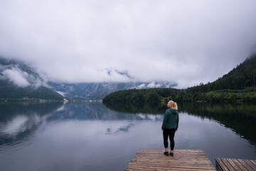 Woman standing on the Hallstatt lake shore enjoying the view of cloudy mountains, Obertraun, Austria