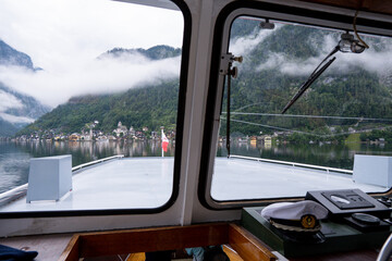 Naklejka premium Ferry window view of famous picturesque Hallstatt village and cloudy mountains on Hallstatt lake, Gmunden, Austria