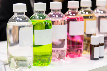 Close-up side view of group of plastic bottles with multi coloured beverages and white blank labels. Soft focus. Copy space. Drinks industry theme.
