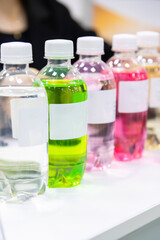 Close-up side view of group of plastic bottles with multi coloured beverages and white blank labels. Soft focus. Copy space. Drinks industry theme.