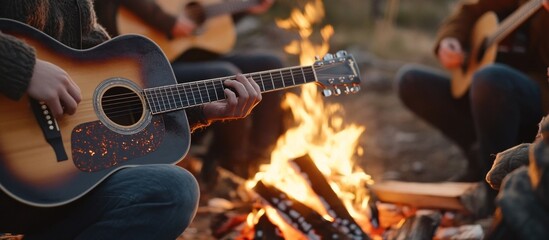 Obraz premium A person plays an acoustic guitar while sitting around a campfire with others.