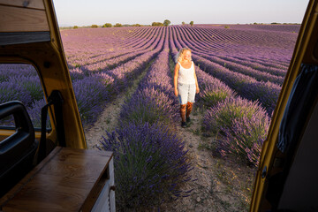 Young blonde woman enjoying the view in her retro yellow camper van at sunrise in Valensole lavender fields in Provence, France