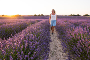 Young blonde woman enjoying a sunrise walk in Valensole lavender fields in Provence, France