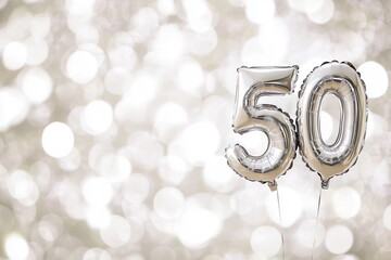 Silver helium floating balloons made in shape of number fifty. Birthday jubilee party or wedding anniversary for 50 years celebration. White and silver bokeh lights background
