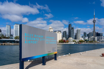 Naklejka premium Toronto, Canada - October 16, 2024: Billy Bishop Toronto City Airport signage with city skyline on the Toronto Islands in Toronto, Ontario, Canada. Billy Bishop Airport (BBTCA) Is a regional airport.