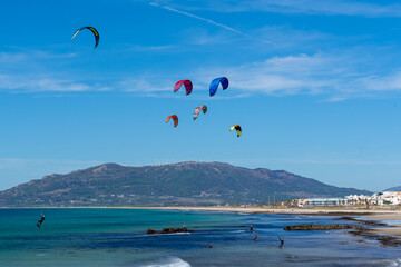 Unrecognized people kitesurfing at the beach with cityscape and mountain in the background in Tangier, Morocco.