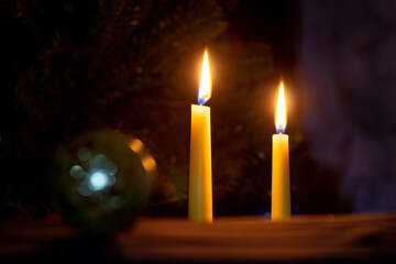two lit candles near the Christmas tree on a dark background