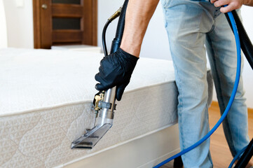 Cleaning concept. Cleaner cleans bed in the bedroom, close up. Virus prevention sanitizing inside. Process of deep furniture cleaning. Professionally chemical cleaning.
