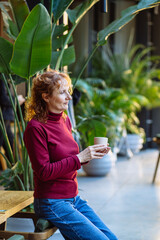 Fototapeta premium Relaxed woman enjoying coffee in indoor garden setting