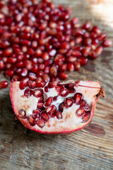 cut piece of fresh pomegranate on a wooden table, against a background of red seeds