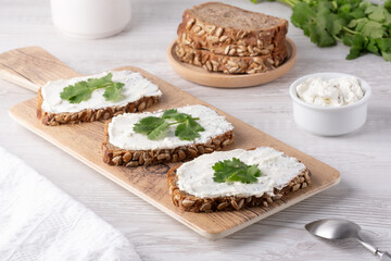 Freshly prepared whole grain bread slices topped with creamy spread and garnished with cilantro on a wooden cutting board