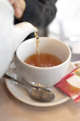 Pouring Freshly Brewed Tea into White Cup: Relaxing Tea Time at Café, Cozy Drink Moment Concept