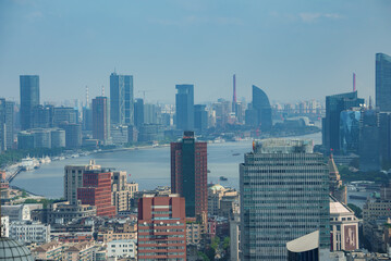 Fototapeta premium View of Shanghai's skyline featuring the Oriental Pearl Tower, historic and modern buildings, and the Huangpu River with active river traffic.