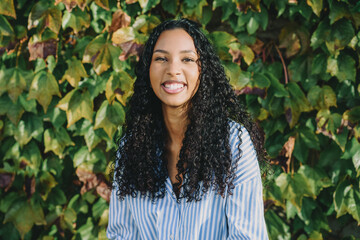 A smiling young woman with curly hair is amid lush green ivy, radiating joy and beauty