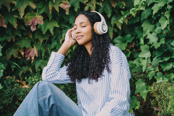 A Young Woman is Enjoying Her Favorite Music with Headphones While Surrounded by Lush Greenery