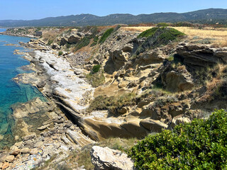 The rocky coastline features layered stone formations and lush green plants along the edge, under a...