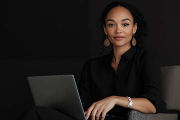 close up of face of an attractive Black woman wearing a black shirt and large earrings, sitting in a chair with a laptop computer in her lap
