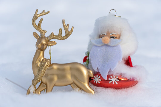 Toy santa claus or ded moroz in christmas clothes riding golden deer on white snow. Xmas and new year holidays decoration. Template for design christmas bauble. Fairy story of festive winter season.