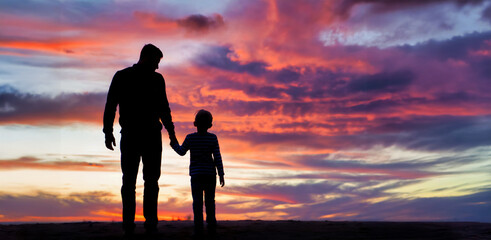 Silhouette of a father and his child at the beach against the background of a beautiful sunset sky. Happy concept of parenting and taking care of children.