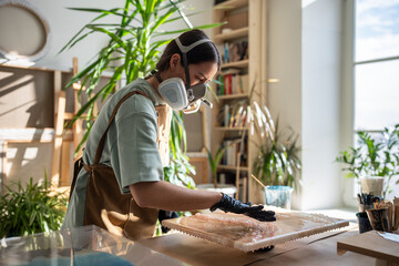 Resin art. Woman artist applying epoxy resin with gloved fingers in art studio workshop. Focused...