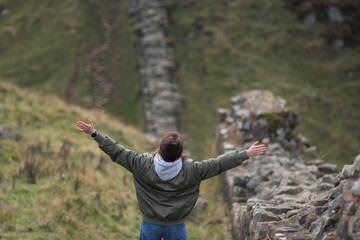 Woman tourist with Hadrian's wall on the background, happy Traveler travel Northumberland, United Kingdom. Destination and Vacation