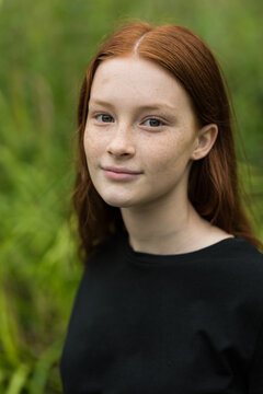 Red haired twelve year old girl with freckles posing with a nature bokeh background