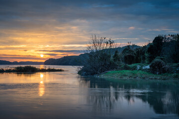 Sunrise idyll landscape on a river with a cloudy sky at golden hour