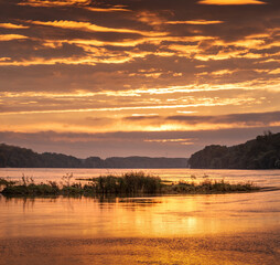 Sunrise idyll landscape on a river with a cloudy sky at golden hour