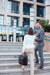 Young male and female businesspeople walking up the stairs and talking in front of an office building