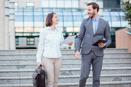 Happy young male and female Caucasian businesspeople walking down the stairs in front of an office building. 