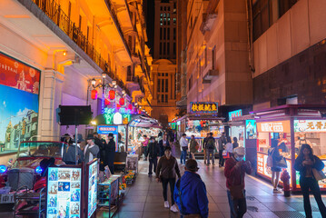 A lively street market in Shanghai, China, illuminated by neon signs and lanterns. People browse stalls amidst modern and traditional architecture.