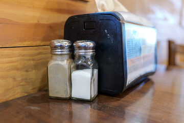 Salt and Pepper shakers next to a napkin dispenser on a wooden cafe table.