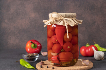 Pickled cherry tomatoes with sweet peppers and garlic in glass jar on brown background