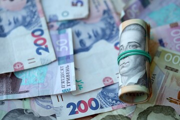 Roll of 500 Ukrainian Hryvnia money bills lies on big pile of ukrainian currency money close up