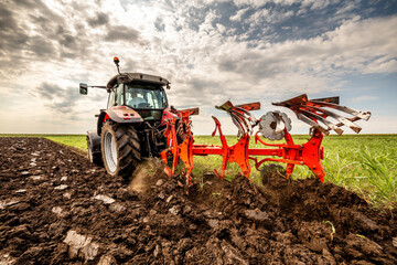Powerful tractor turns the soil, readying the field for planting under a dramatic sky