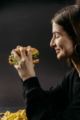 Side profile of woman savoring delicious burger, capturing joy of indulgent dining with fries nearby