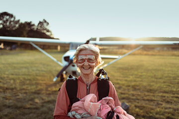 Senior woman smiling after skydiving with airplane in background