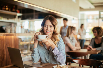 Young woman having a cup of coffee in a cafe while using a laptop