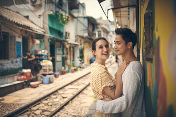 Fototapeta premium City, tramway and couple in portrait on vacation, travel adventure and exploring for anniversary. Interracial marriage, woman and man with smile for admiration, hug and bonding outdoor in Vietnam