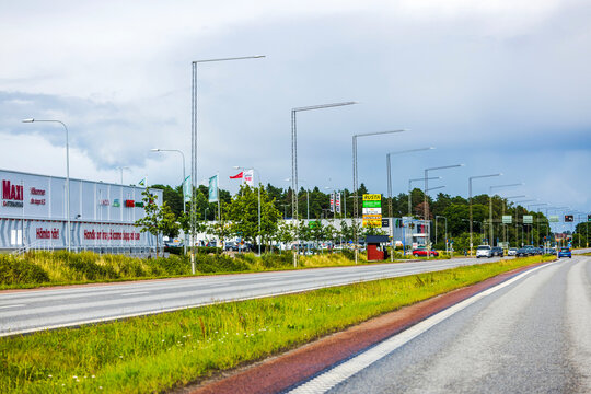 Roadside view of commercial stores and signage in suburban area with trees and parked cars in background. Sweden. 