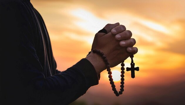 Man's hands pray to hold a bead rosary with Jesus Christ on the cross or the Crucifix with sunset. Christian Catholic religious faith holding a black rosary and praying.