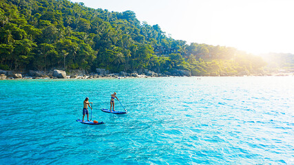 Couple, paddle board and ocean in summer, outdoor and drone on holiday, island and adventure in...